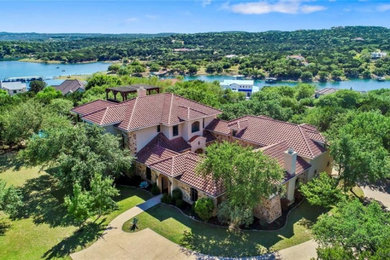 Example of a huge tuscan beige three-story stone house exterior design in Austin with a hip roof and a tile roof
