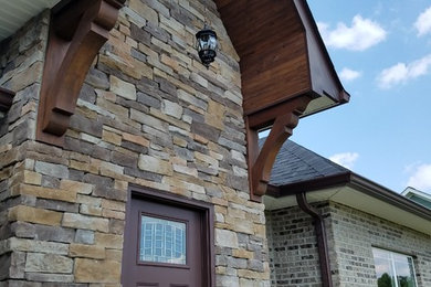 На фото: одноэтажный, коричневый дом с облицовкой из камня и двускатной крышей с