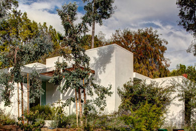 Example of a large mid-century modern white one-story stucco exterior home design in Los Angeles with a mixed material roof
