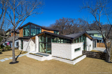 Mid-sized mid-century modern white two-story stone house exterior photo in Austin with a metal roof