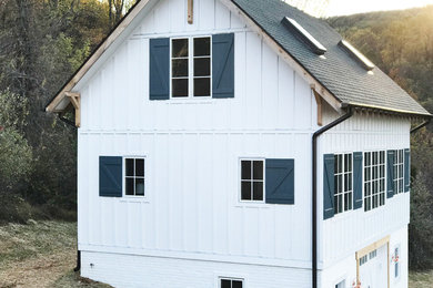 Diseño de fachada de casa blanca campestre de tres plantas con revestimiento de aglomerado de cemento y tejado de teja de madera