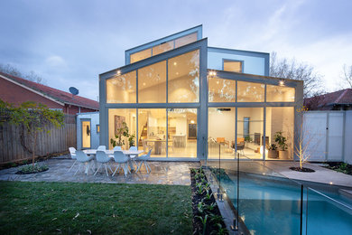 Cette photo montre une façade de maison grise en verre de taille moyenne et à un étage avec un toit à deux pans et un toit mixte.