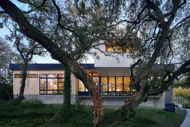 Inspiration for a large mid-century modern white two-story stucco exterior home remodel in Austin with a mixed material roof