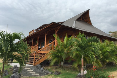 Imagen de fachada de casa beige tropical de tamaño medio de dos plantas con revestimiento de madera y tejado de metal