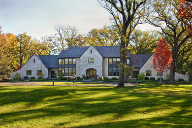 На фото: огромный, двухэтажный, бежевый частный загородный дом в классическом стиле с облицовкой из камня, двускатной крышей и крышей из гибкой черепицы