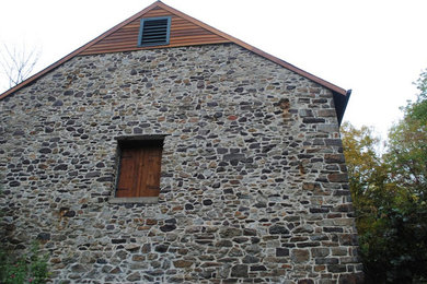 Example of a mid-sized farmhouse gray stone gable roof design in Philadelphia