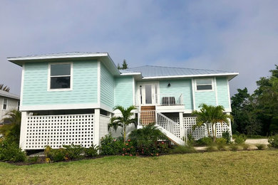 Modelo de fachada de casa azul y gris costera de tamaño medio de una planta con revestimiento de aglomerado de cemento, tejado a cuatro aguas y tejado de metal