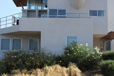 Large minimalist beige three-story stucco flat roof photo in San Diego