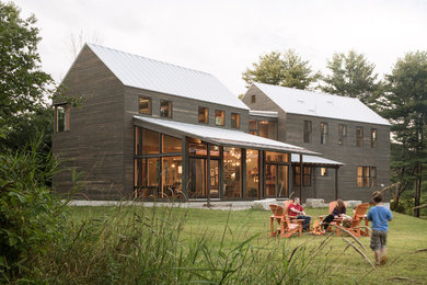 Immagine della villa marrone country con rivestimento in legno, tetto a capanna e copertura in metallo o lamiera