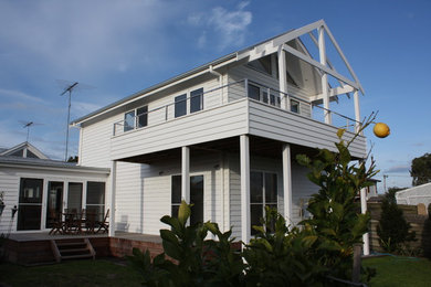 Modelo de fachada blanca marinera de tamaño medio de dos plantas con revestimiento de madera y tejado a dos aguas