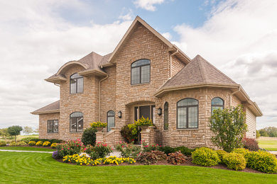 Example of a large classic beige two-story stone house exterior design in Milwaukee with a hip roof and a shingle roof