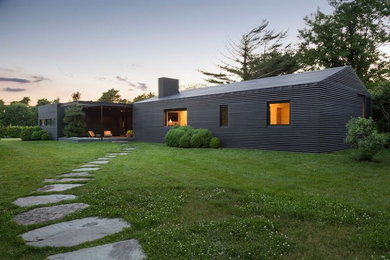 Cette image montre une grande façade de maison noire en bois de plain-pied avec un toit à deux pans et un toit en métal.