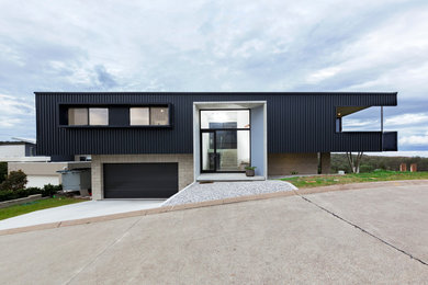 Modelo de fachada de casa negra moderna de tamaño medio de dos plantas con revestimiento de metal, tejado plano y tejado de metal