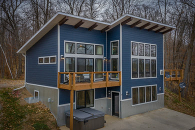 Diseño de fachada de casa azul moderna de tamaño medio de dos plantas con revestimiento de aglomerado de cemento, tejado de un solo tendido y tejado de teja de madera