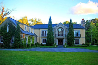 Huge transitional yellow two-story stucco exterior home photo in New York with a shingle roof