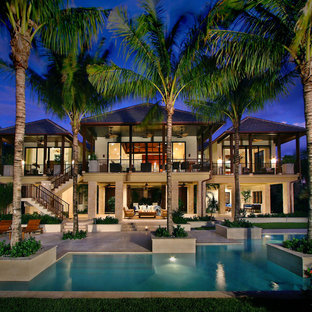 Large tropical beige two-story concrete house exterior idea in Miami with a hip roof and a shingle roof