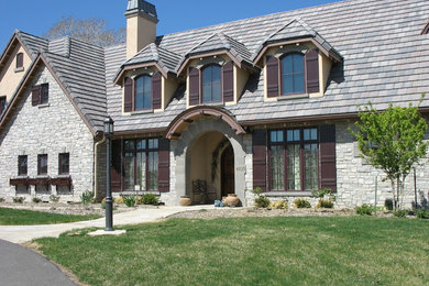 Diseño de fachada de casa gris tradicional grande de dos plantas con revestimiento de piedra, tejado a la holandesa y tejado de teja de barro