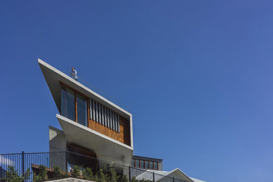 Photo of a large and gey modern concrete detached house in Brisbane with three floors, a flat roof and a mixed material roof.