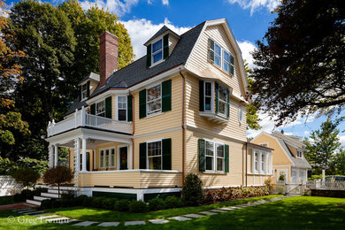 This is an example of a large and yellow classic house exterior in Boston with three floors, wood cladding and a mansard roof.