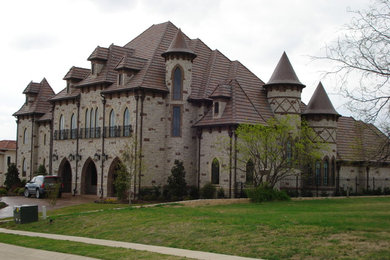 Huge ornate brown three-story stone house exterior photo in Dallas with a clipped gable roof and a tile roof