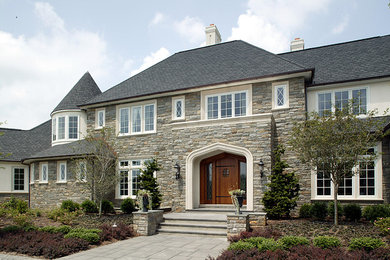 Inspiration for a large timeless gray two-story stone house exterior remodel in Other with a hip roof and a shingle roof