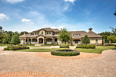 Huge traditional beige two-story stucco house exterior idea in Houston with a hip roof and a shingle roof