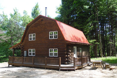 Immagine della facciata di una casa marrone rustica a due piani con rivestimento in legno e tetto a mansarda