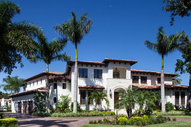 Large tuscan white two-story stucco house exterior photo in Tampa with a hip roof and a tile roof