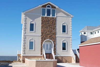 Modelo de fachada de casa beige costera grande de tres plantas con revestimientos combinados, tejado a dos aguas y tejado de teja de madera