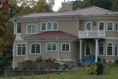 Foto della villa ampia beige classica a tre piani con rivestimento in stucco, tetto a padiglione e copertura in tegole