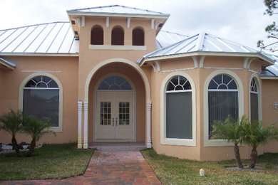 Modelo de fachada de casa beige mediterránea grande de dos plantas con revestimiento de estuco y tejado de metal