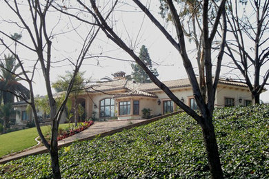 Diseño de fachada de casa beige y marrón mediterránea grande de una planta con revestimiento de estuco, tejado a cuatro aguas y tejado de teja de barro