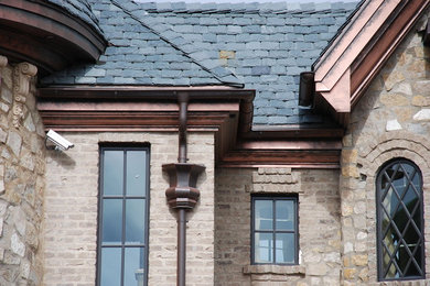 На фото: огромный, коричневый частный загородный дом в стиле кантри с разными уровнями, облицовкой из камня, полувальмовой крышей и крышей из гибкой черепицы с