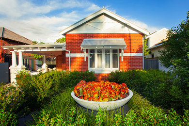 Imagen de fachada de casa roja clásica de tamaño medio de una planta con revestimiento de ladrillo, tejado a dos aguas y tejado de metal