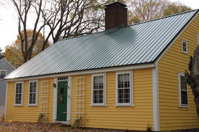 На фото: маленький, двухэтажный, желтый частный загородный дом в стиле кантри с двускатной крышей и металлической крышей для на участке и в саду