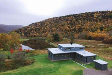 Cette photo montre une façade de maison bleue moderne en bois de taille moyenne et à un étage avec un toit en appentis et un toit en métal.