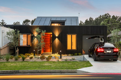 Modelo de fachada de casa negra nórdica de tamaño medio de dos plantas con revestimiento de madera y tejado de metal