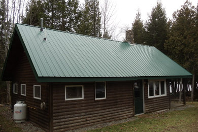 Foto de fachada de casa marrón rústica grande de una planta con revestimiento de madera, tejado a dos aguas y tejado de metal
