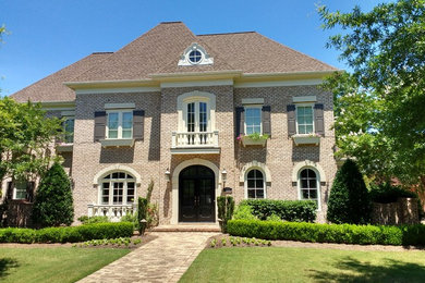 Inspiration for a large contemporary beige two-story brick house exterior remodel in Charlotte with a hip roof and a shingle roof