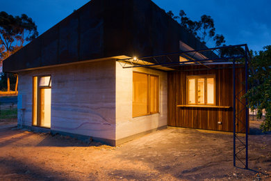 Diseño de fachada de casa beige actual de tamaño medio de una planta con revestimiento de adobe, tejado plano y tejado de metal