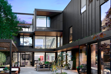 На фото: большой, трехэтажный, черный частный загородный дом в современном стиле с облицовкой из металла, плоской крышей и зеленой крышей с
