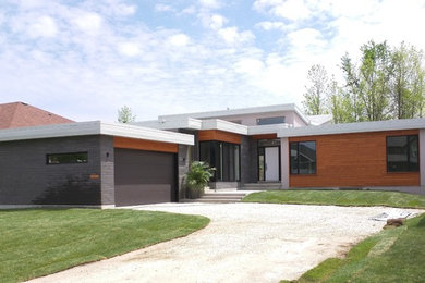 Imagen de fachada de casa gris actual grande de una planta con revestimientos combinados y tejado plano