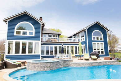 Diseño de fachada de casa azul costera grande de dos plantas con revestimiento de aglomerado de cemento, tejado a dos aguas y tejado de teja de barro