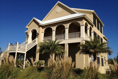 Modelo de fachada de casa beige costera grande de dos plantas con revestimiento de estuco, tejado a dos aguas y tejado de metal