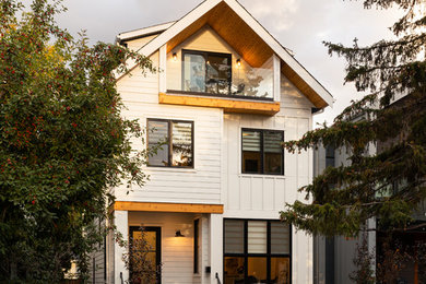 Modelo de fachada de casa blanca campestre de tamaño medio de tres plantas con revestimiento de aglomerado de cemento y tejado de teja de madera