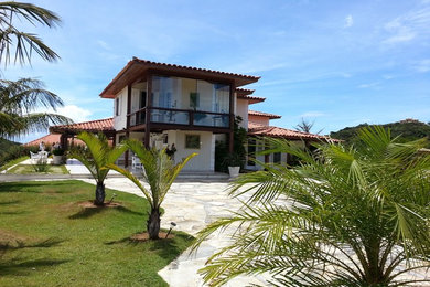 Foto de fachada de casa beige y roja tropical de tamaño medio de dos plantas con tejado a cuatro aguas y tejado de teja de barro