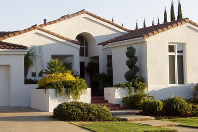 Пример оригинального дизайна: одноэтажный, белый частный загородный дом среднего размера в средиземноморском стиле с облицовкой из цементной штукатурки, двускатной крышей и черепичной крышей