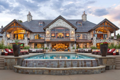 This is an example of an expansive rustic house exterior in Denver with three floors, stone cladding and a pitched roof.