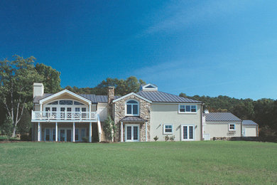Cette photo montre une grande façade de maison beige chic en stuc à un étage avec un toit à deux pans et un toit en métal.