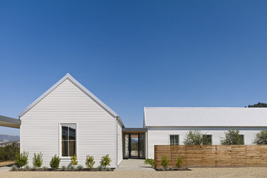 Foto della facciata di una casa grande bianca country a un piano con rivestimento in legno e tetto a capanna